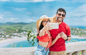 Happy Young tourist couple taking a selfie in a beautiful viewpoint. Smiling tourist couple taking a selfie at the viewpoint of San Juan del Sur