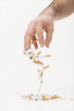 Close up hand throwing broken cigarettes against white background