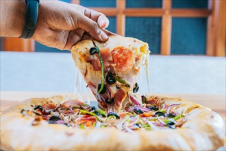Hand taking a delicious slice of supreme pizza with vegetables. Hand taking a slice of supreme pizza on wooden table
