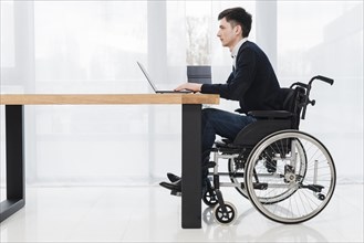 Side view young businessman sitting wheelchair using laptop new office