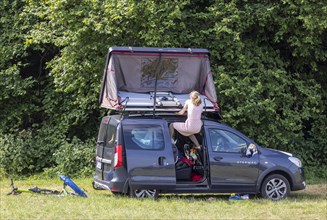 Roof tent on a Dacia Stepway. A young woman struggles to unfold the tent