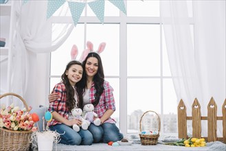 Mother daughter sitting together holding stuffed bunny easter celebration