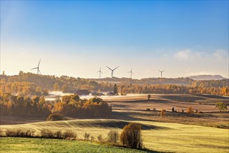 Landscape view with autumn fog by the fields and farms and wind turbines on the horizon
