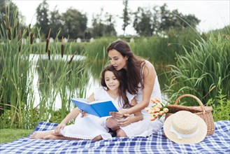 Mother daughter reading book by lake