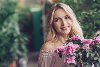 Smiling blonde young woman standing front flowering plants