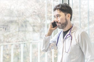 Latino doctor talking on the phone looking out the window