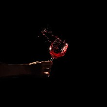 Person s hand holding glass red wine splashing out glass
