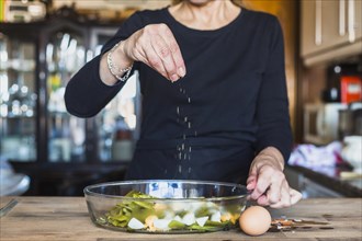 Crop hands elderly woman sprinkling dish salt