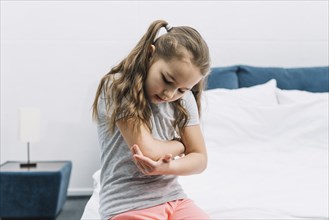 Portrait girl sitting white bed looking her injured elbow