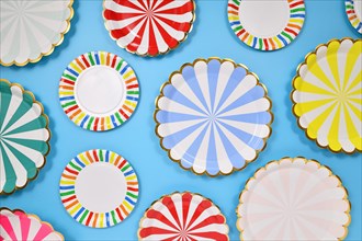 Different colorful striped paper party plates on blue background