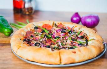 Close up of supreme pizza with olives and vegetables on wooden table. Delicious supreme pizza with vegetables served on table