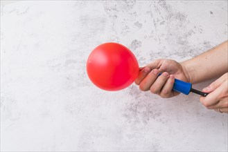 Close up hand blowing red balloon with pump against wall