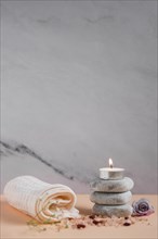 Lighted candle spa stones with napkin rose himalayan salts peach colored backdrop against grey background
