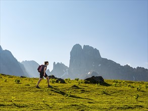 Woman hiking across alpine meadow in front of the peaks of the Bischofsmuetze
