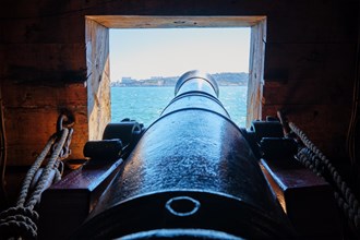 Sea view out of a gunport over the gun cannon muzzle on the gun deck of a Age of Sail sailing ship