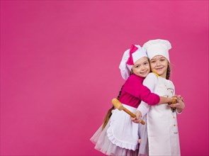 Two girls cooks kitchen utensils hugging