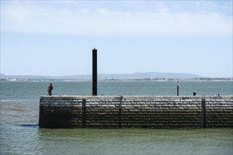A person sits on a quay wall at the port of Lisbon