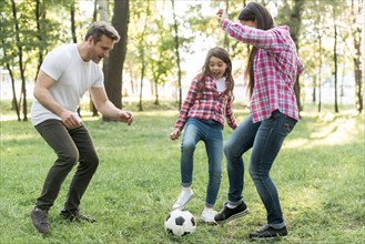 Cheerful girl playing soccer ball with her parent grass park