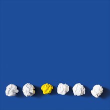 Yellow crumpled paper ball among white balls against blue background