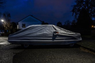 Covered car parked on the street under a lamppost at night