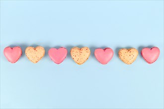 Pink and yellow heart shaped French macaron sweets in a row on blue background