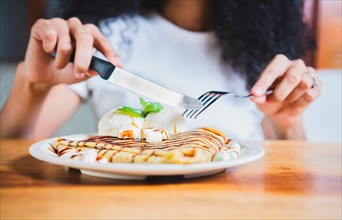 Woman hands eating chocolate crepe and ice cream with fork. Close up of woman eating a chocolate crepe with fork