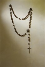 A prayer chain with a cross hangs on a wall