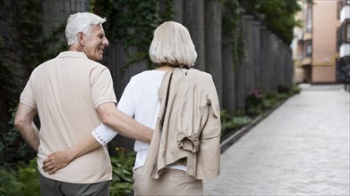 Back view embraced older couple taking walk outdoors