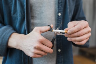 Close up man s hand cutting cigarette with scissor