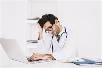 Confused young male doctor using laptop