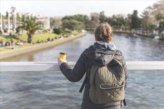 Back view of a woman on a bridge contemplating the river while having a coffee