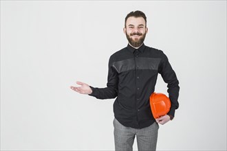 Smiling male engineer holding hardhat shrugging