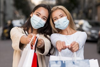 Two women with medical masks posing together with shopping bags