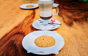 Close up of biscuit with cappuccino on wooden table. Delicious glass of hot cappuccino with cookie on wooden background