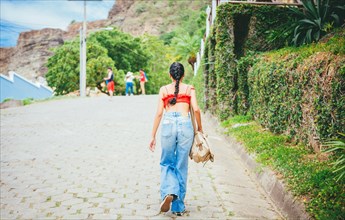 Rear view of tourist girl walking on the street. Back view of tourist woman going up a hill in street