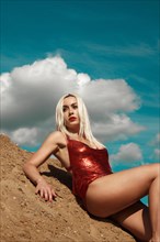 Beautiful blond woman in a red sexy dress on the background of the sky and sand. Beauty of the body and face