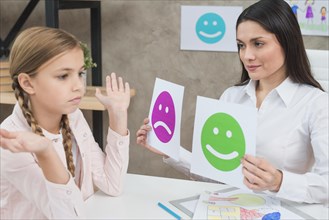 Smiling psychologist showing happy sad emotion faces cards girl child