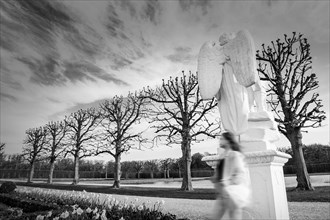 Ghost in the park. Black and white photography. A defocused person against the background of a moody sky and a sculpture of an angel. Dramatic poetic background. Copy space