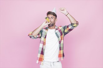 Man raising his arms while blowing party horn pink background