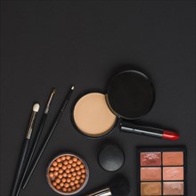 Overhead view makeup products with brushes black backdrop