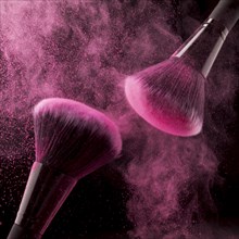 Two cosmetic brushes pink powder dark background