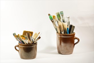 Artistic brushes and painting tools in old ceramic pots on white neutral background