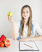 Young female dietician holding green apple with food clipboard desk