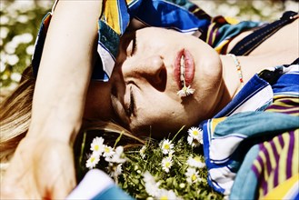 Pretty young woman lying in the grass between daisies with a daisy in her mouth
