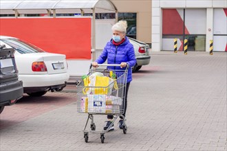 Shot of mature woman wearing protective mask with shopping cart on the parking lot during coronavirus pandemic. Everyday life