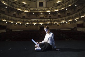 Side view female mime sitting stage reading manuscript