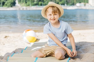 Smiling boy sitting mat sand shore