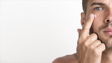 Half face shirtless young man applying cream his face against white background