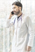 Latino doctor talking on the phone looking out the window