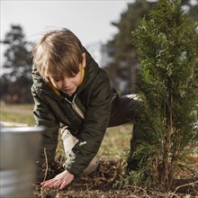 Front view young boy planting tree outdoors